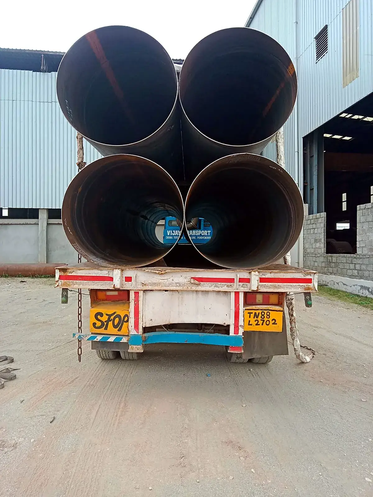 Four very large diameter pipes on a trailer outside a factory